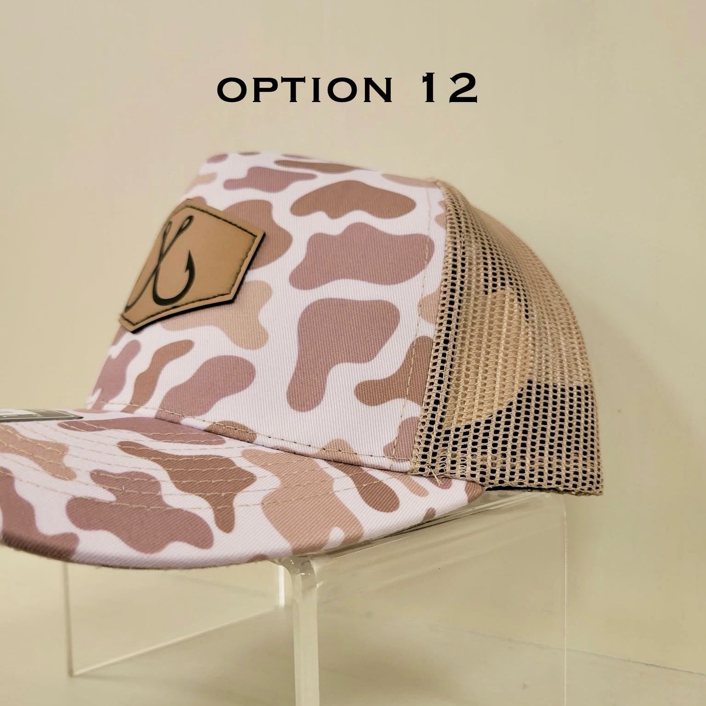 Camouflage-patterned cap with mesh back on a clear stand against a beige background