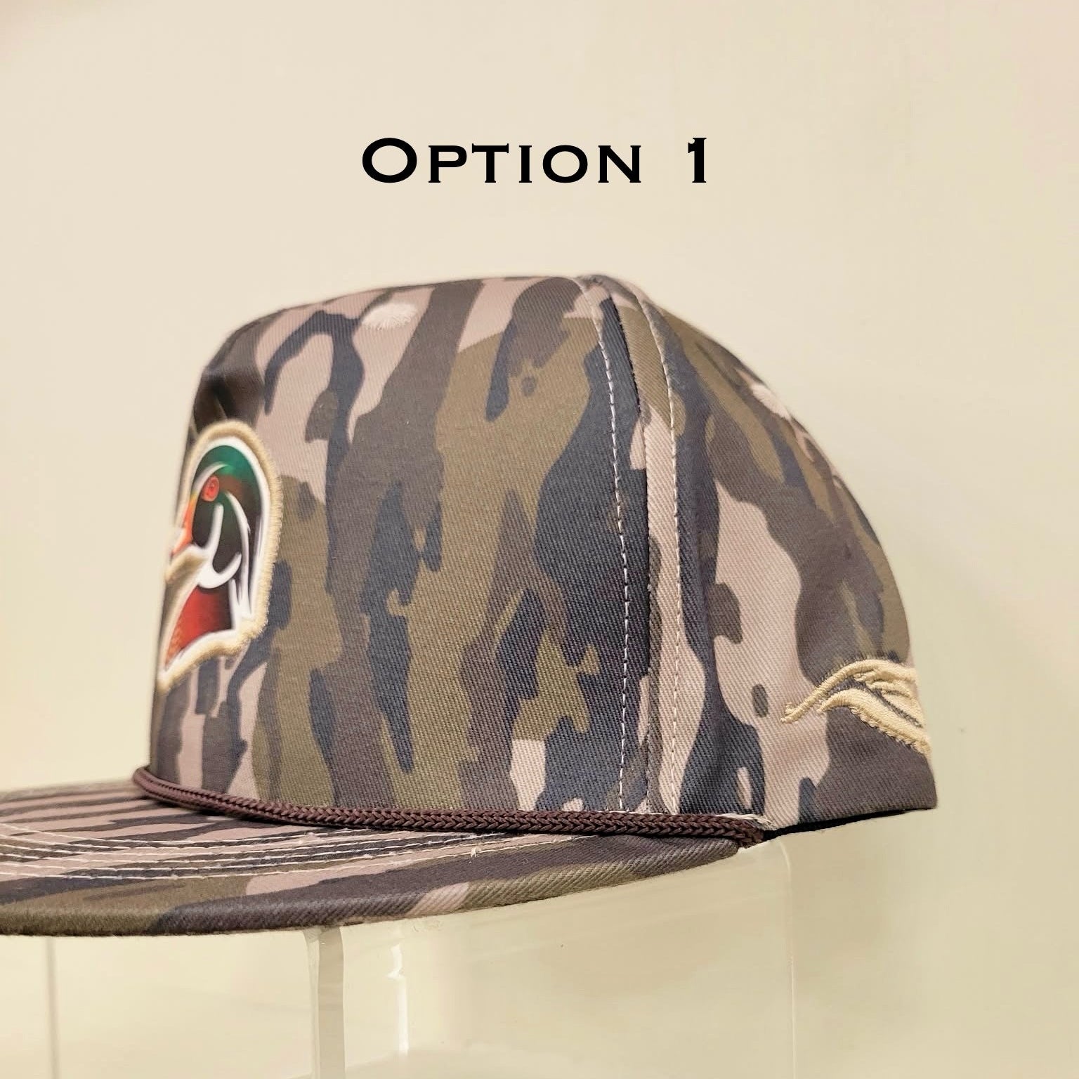 Camouflage baseball cap with a logo on a clear stand against a beige background