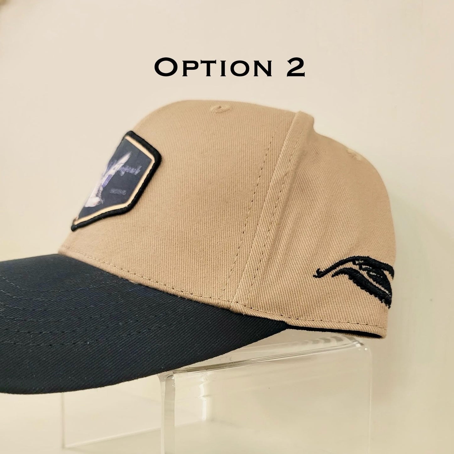 Beige and black cap with a patch on a clear stand against a beige background