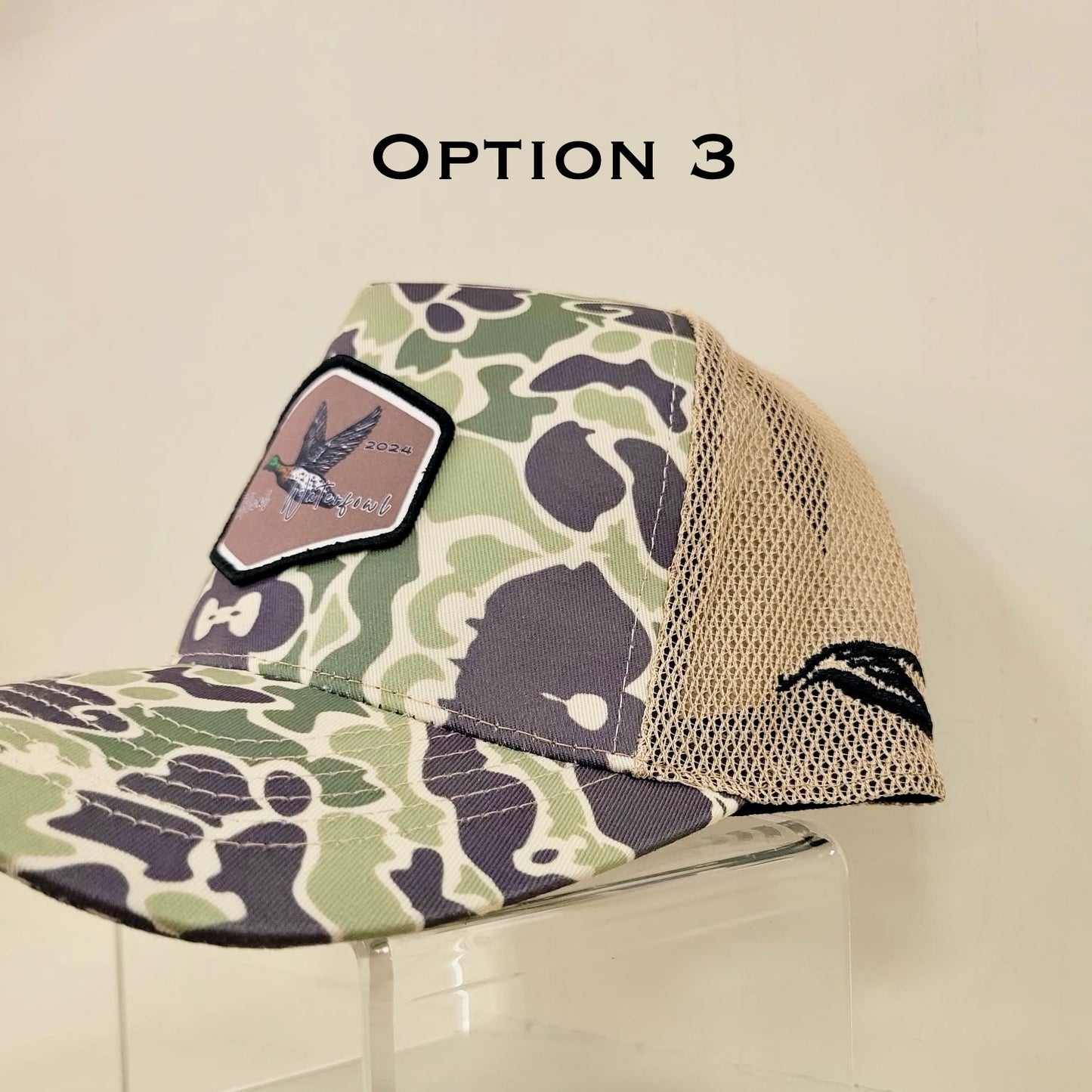 Camouflage-patterned cap with mesh back on a clear stand against a beige background