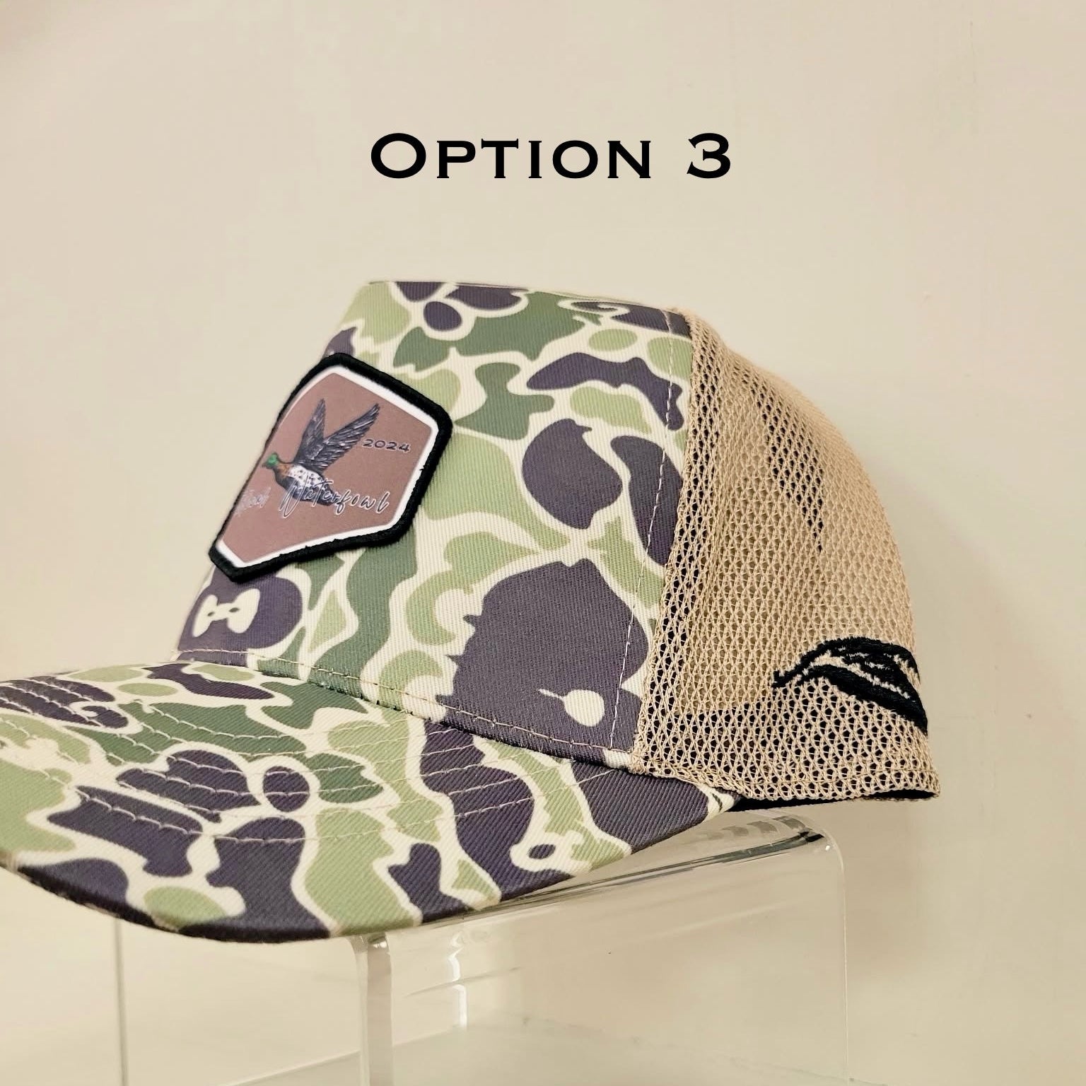 Camouflage-patterned cap with mesh back on a clear stand against a beige background